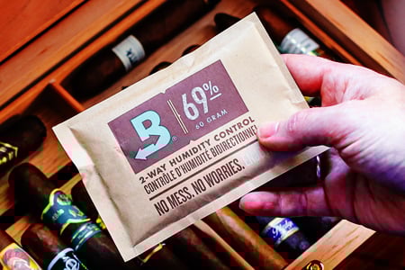 Male hand holding a 69% RH Boveda and placing it in a hood humidor with cigars